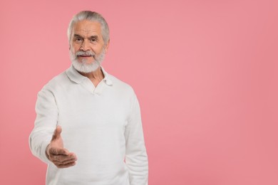 Photo of Senior man welcoming and offering handshake on pink background, space for text