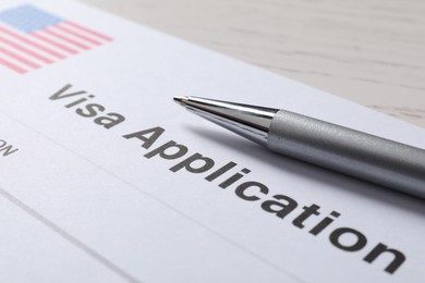 Photo of Immigration to USA. Visa application form and pen on white wooden table, closeup