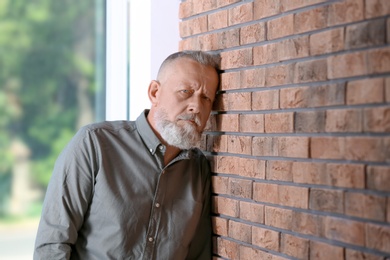 Photo of Senior man in state of depression near brick wall