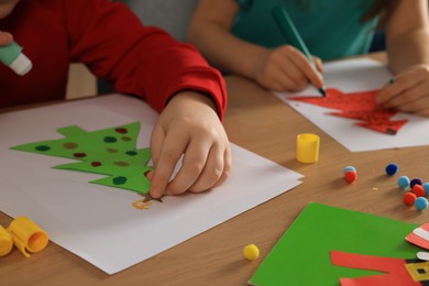 Photo of Little children making beautiful Christmas greeting cards at wooden table, closeup