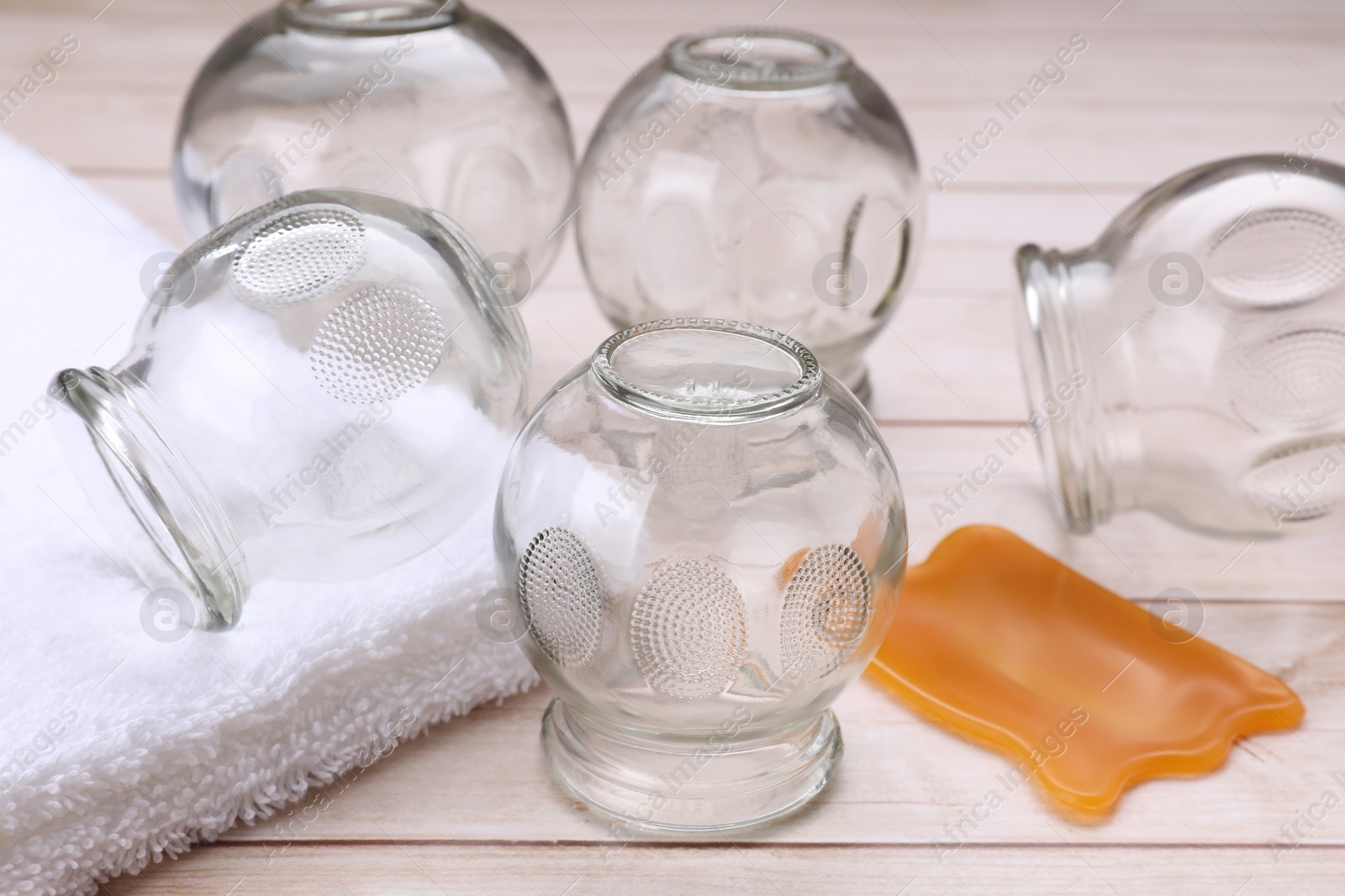 Photo of Glass cups, towel and gua sha on white wooden table, closeup. Cupping therapy