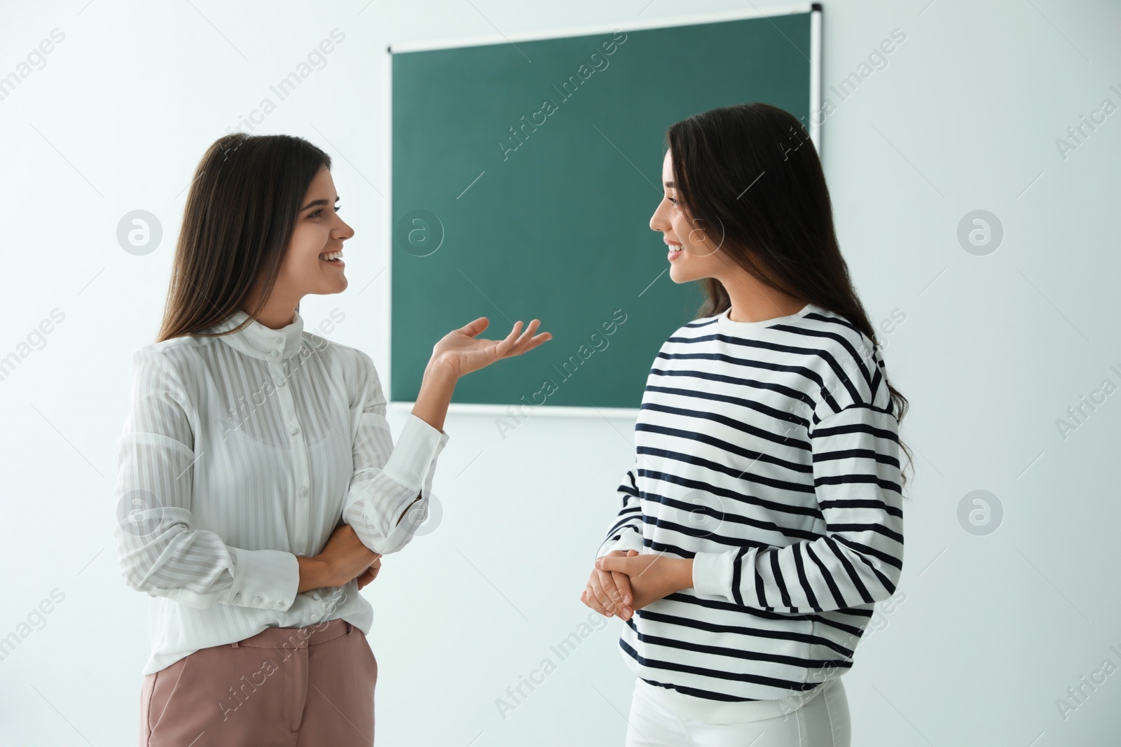 Photo of Young women talking near green chalkboard in classroom