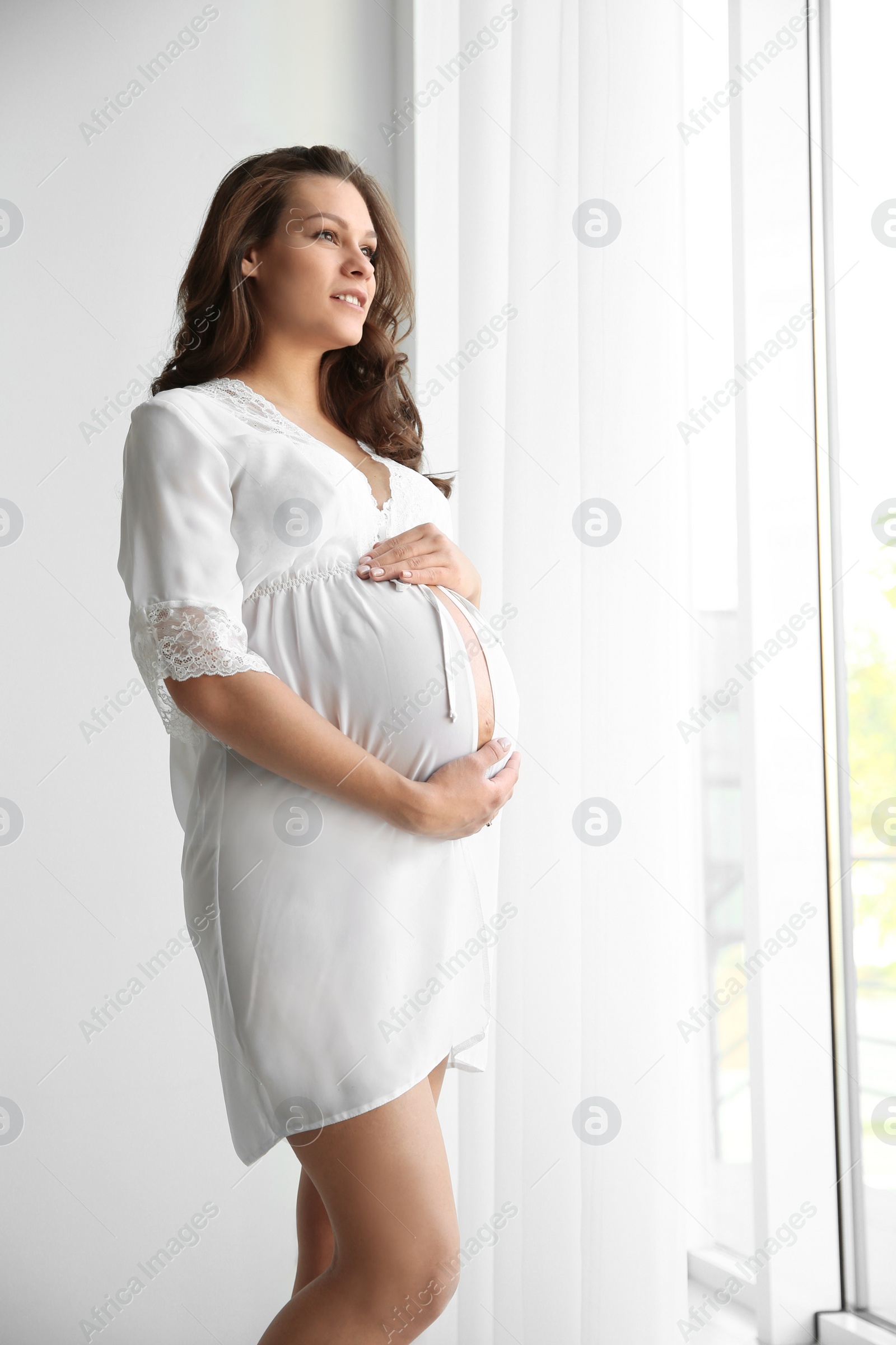 Photo of Young pregnant woman in lace nightgown near window indoors. Space for text