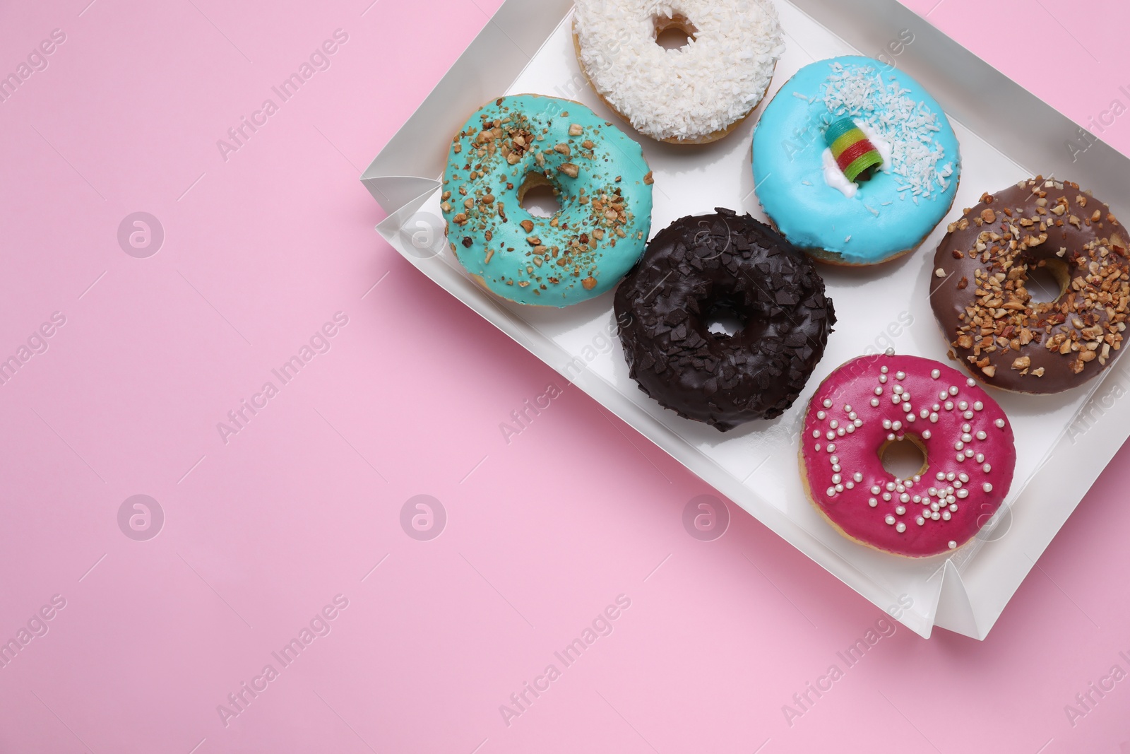 Photo of Box with different tasty glazed donuts on pink background, top view. Space for text