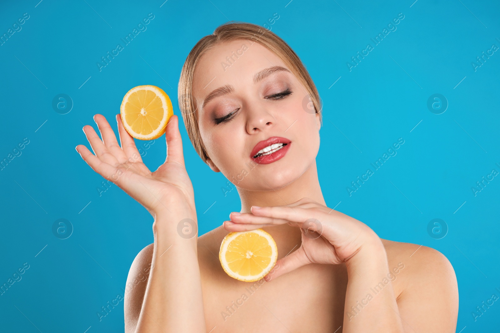 Photo of Young woman with cut lemon on blue background. Vitamin rich food