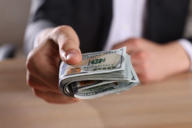 Money exchange. Man holding dollar banknotes at wooden table, closeup