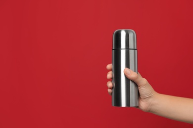 Photo of Woman holding modern thermos on red background, closeup. Space for text