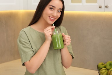 Photo of Beautiful young woman drinking delicious smoothie in kitchen