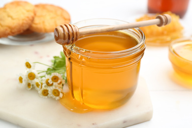 Photo of Tasty honey and chamomile flowers on light marble board, closeup