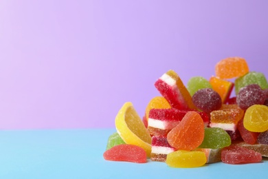 Photo of Pile of delicious bright jelly candies on violet background. Space for text