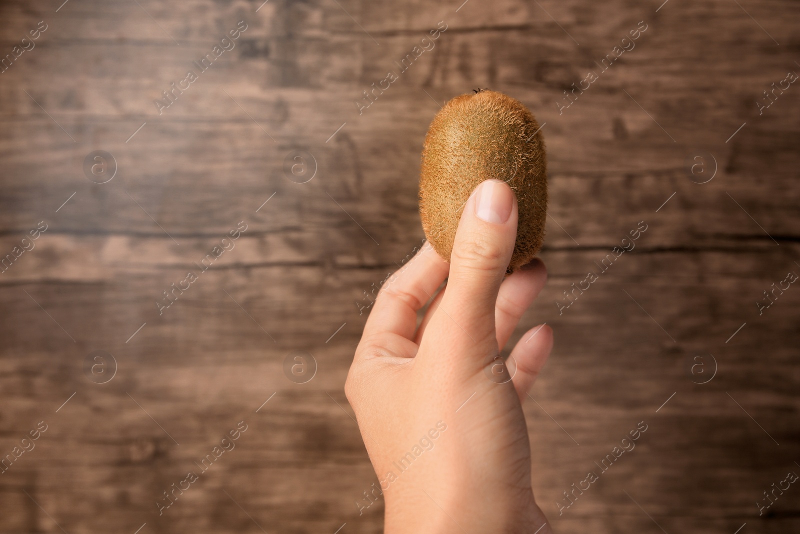 Photo of Woman holding delicious fresh kiwi on wooden background, closeup. Space for text