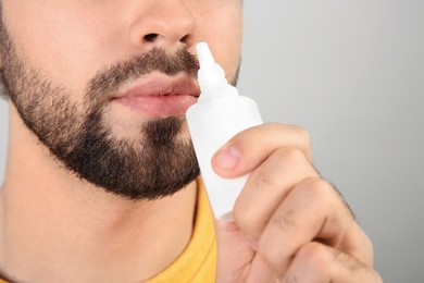 Man using nasal spray on light grey background, closeup. Space for text