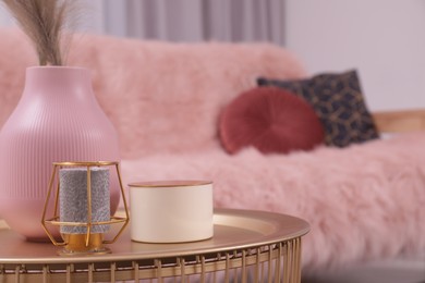 Vase and candles on coffee table near sofa in stylish room, closeup. Interior design