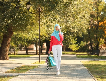 Muslim woman with shopping bags talking on phone in park