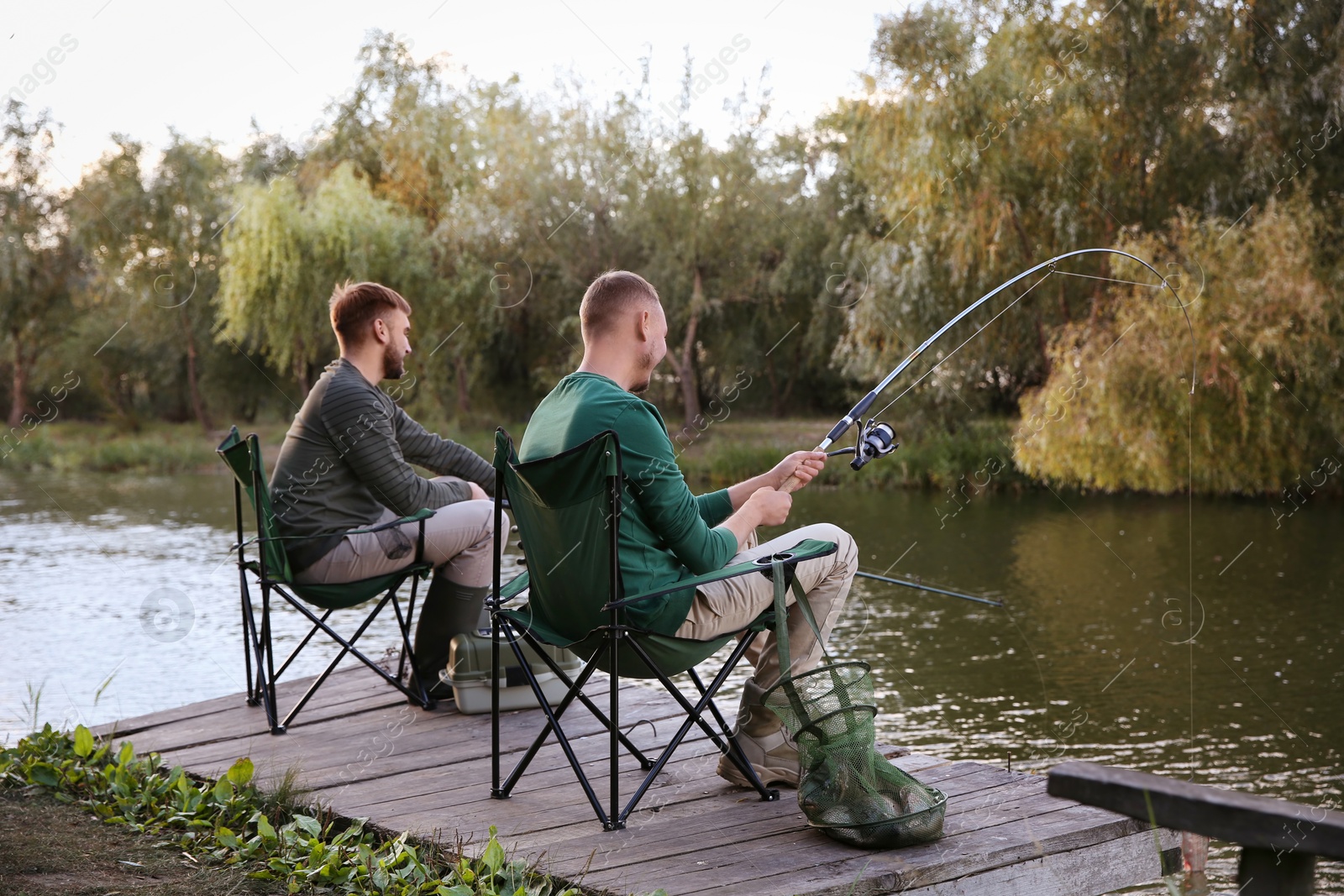 Photo of Friends fishing on wooden pier at riverside. Recreational activity