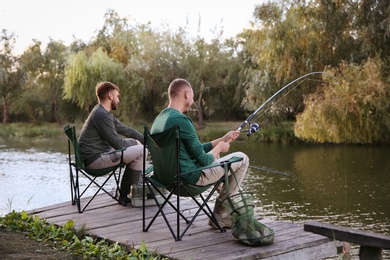 Photo of Friends fishing on wooden pier at riverside. Recreational activity