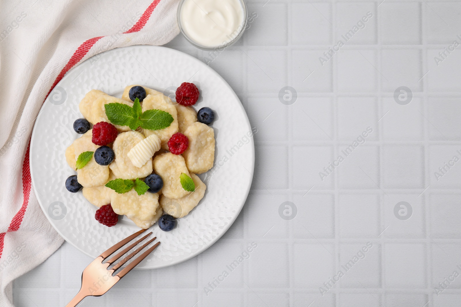 Photo of Plate of tasty lazy dumplings with berries, butter and mint leaves on white tiled table, flat lay. Space for text