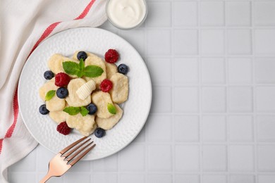 Photo of Plate of tasty lazy dumplings with berries, butter and mint leaves on white tiled table, flat lay. Space for text