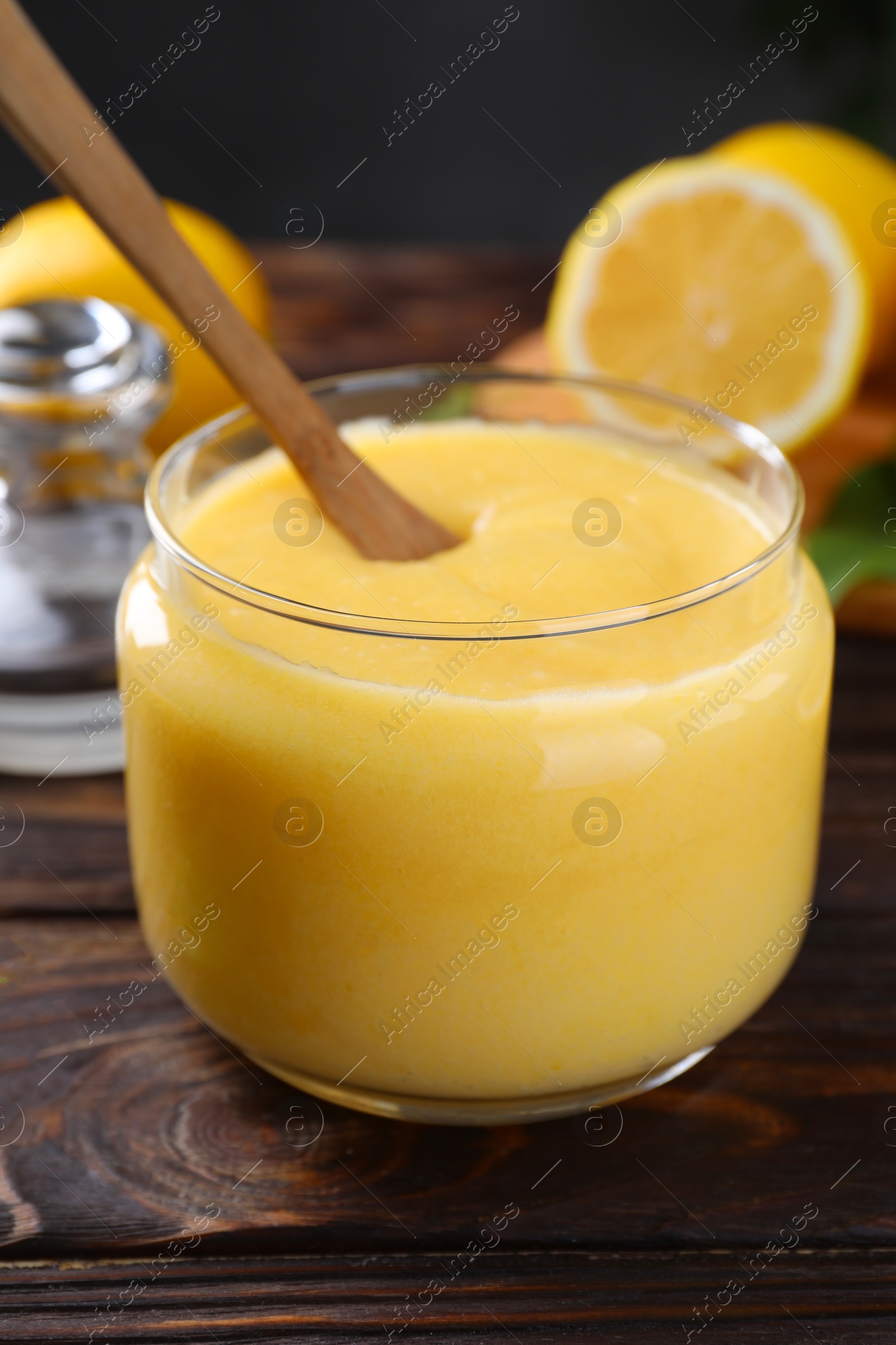 Photo of Delicious lemon curd in glass jar and spoon on wooden table