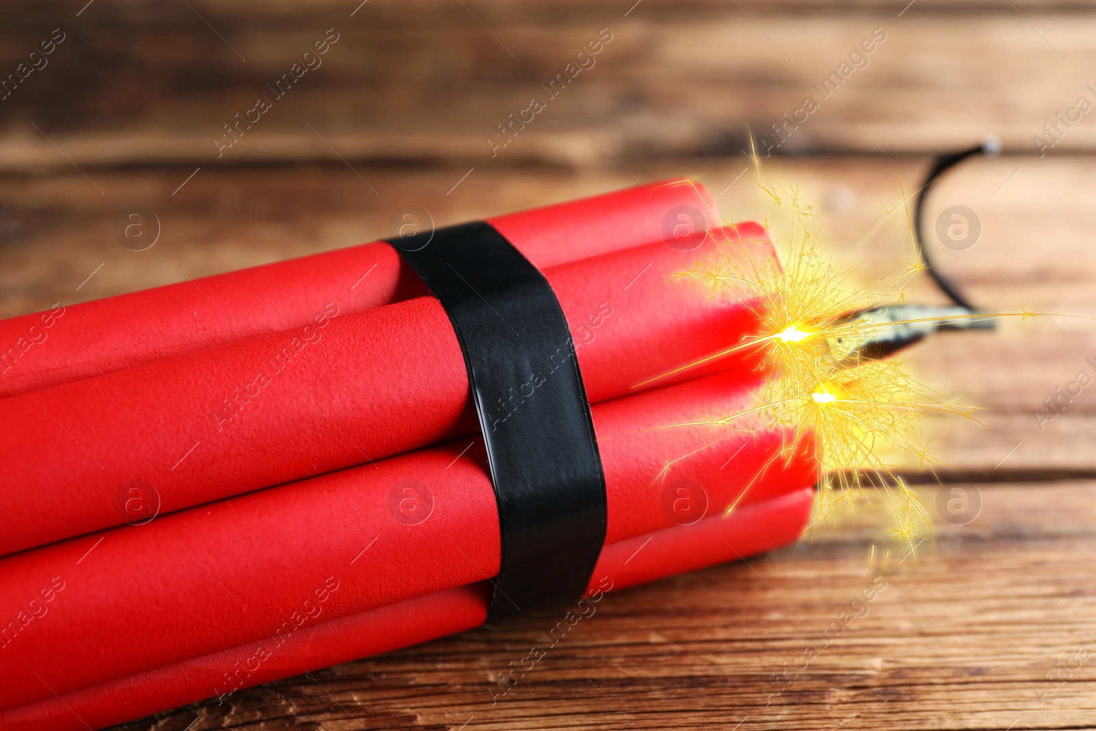 Image of Dynamite bomb with lit fuse on wooden table, closeup