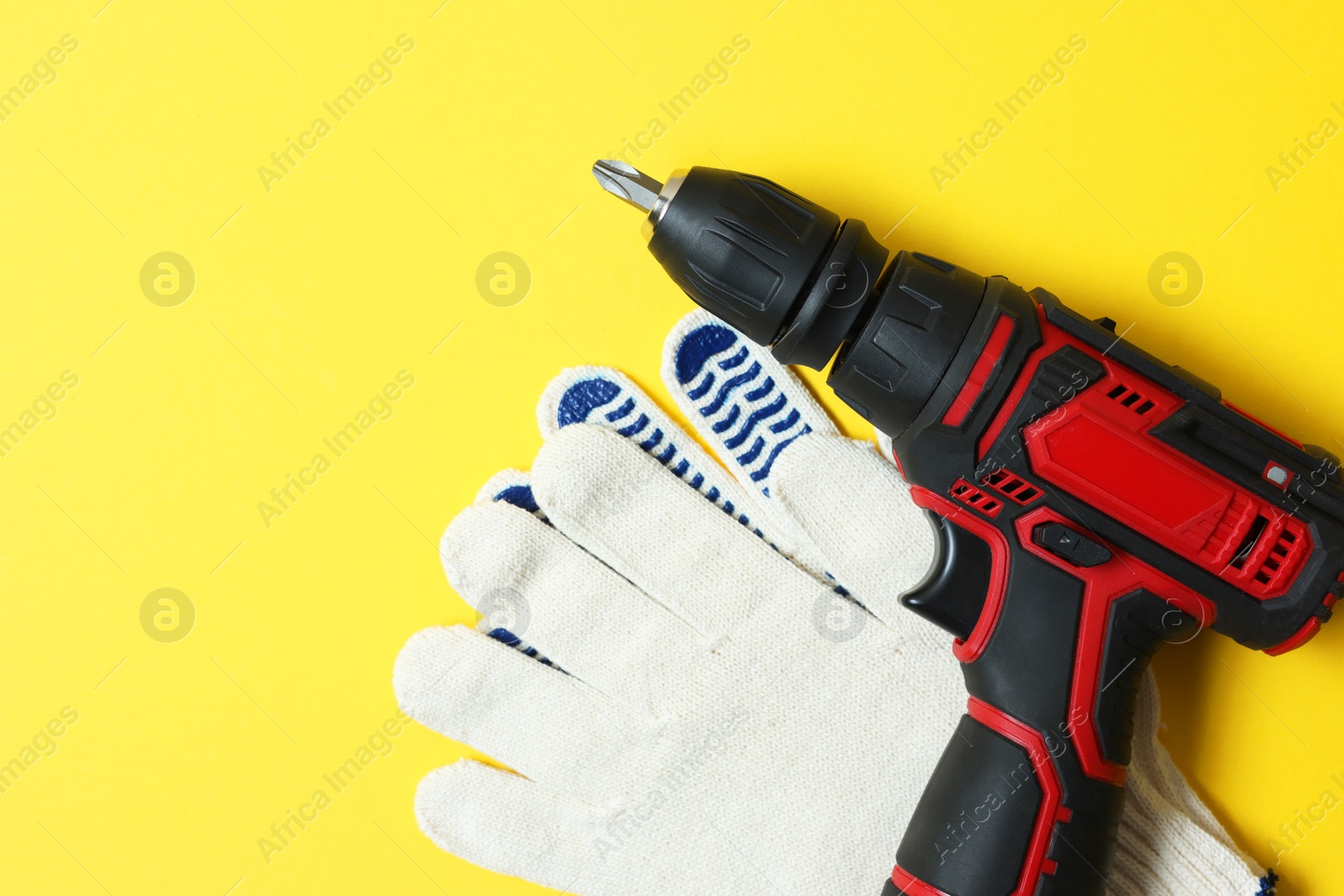 Photo of Electric screwdriver, bit set and gloves on yellow background, flat lay