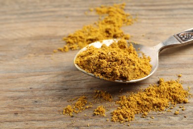 Photo of Spoon with dry curry powder on wooden table, closeup. Space for text