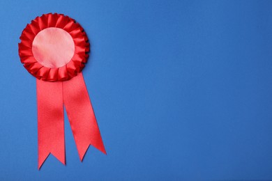 Photo of Red award ribbon on blue background, top view. Space for text