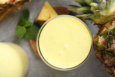 Photo of Tasty pineapple smoothie, mint and fruit on grey textured table, flat lay