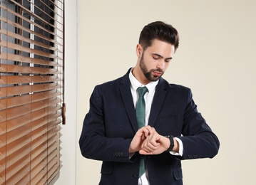 Portrait of confident businessman checking time at window indoors