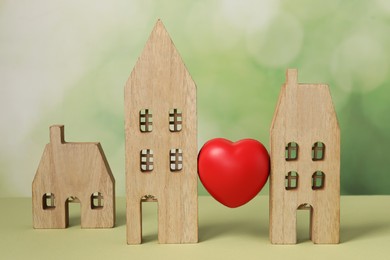 Photo of Long-distance relationship concept. Decorative heart between two wooden house models on light green background