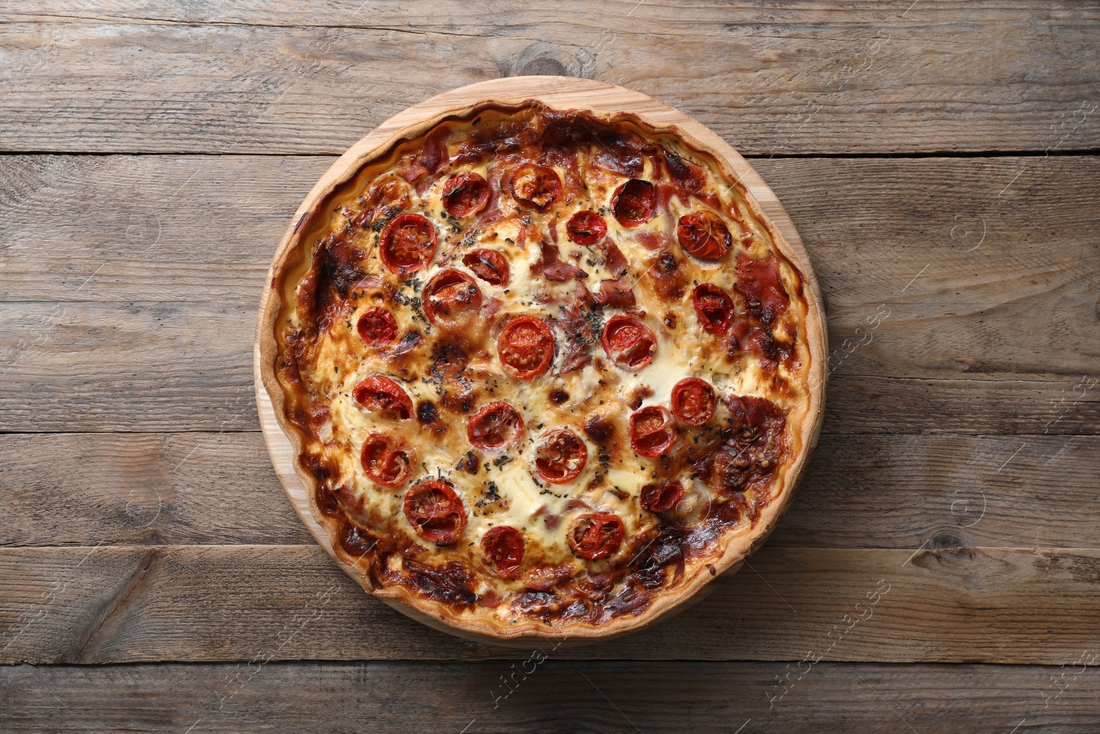 Photo of Delicious homemade quiche with prosciutto and tomatoes on wooden table, top view