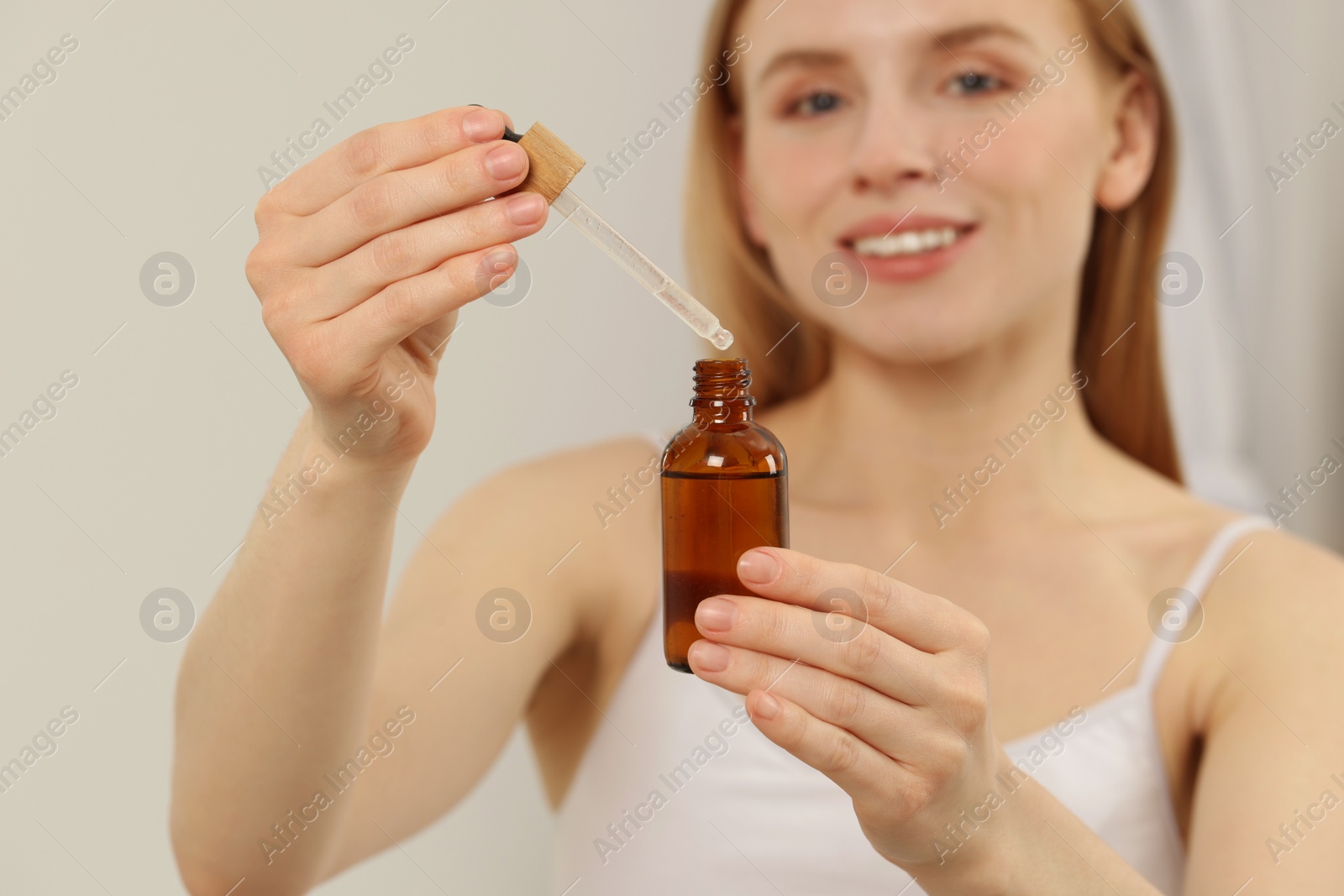 Photo of Woman with bottle of essential oil on blurred background, selective focus