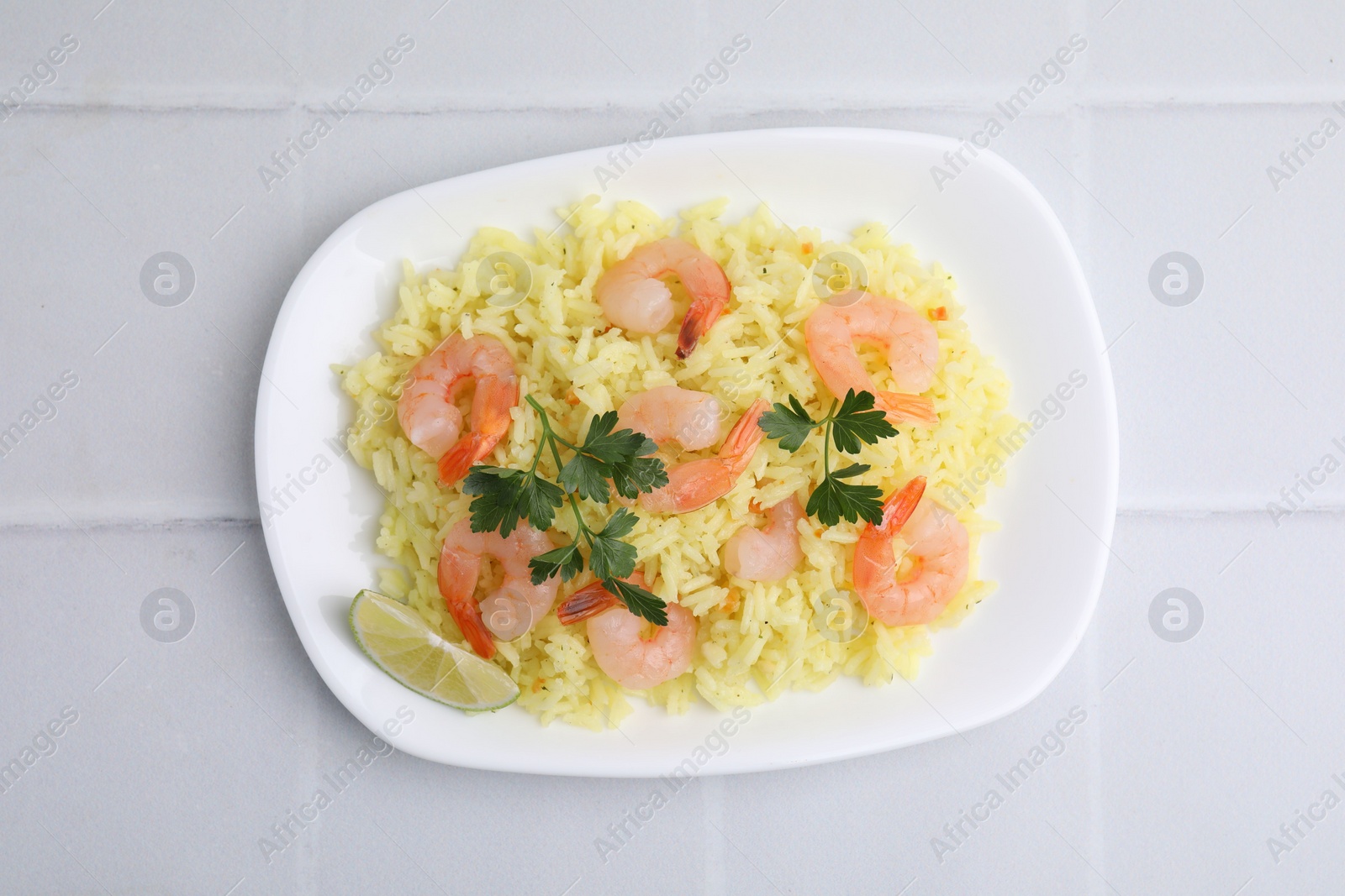 Photo of Delicious risotto with shrimps, lime and parsley on white tiled table, top view