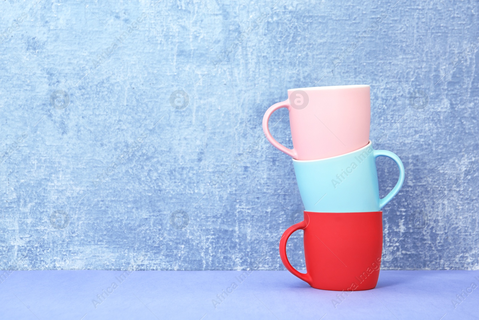 Photo of Different colorful cups on table against color background