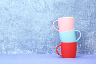 Different colorful cups on table against color background