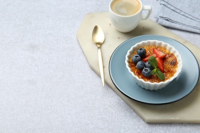 Delicious creme brulee with berries and mint in bowl served on grey textured table. Space for text