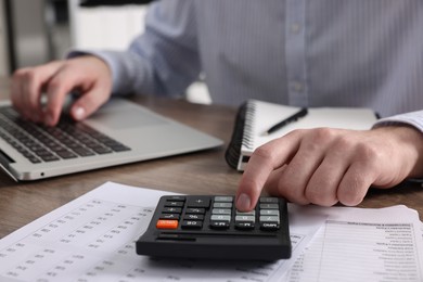 Man using calculator while working on laptop at table, closeup