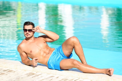 Handsome young man lying near swimming pool on sunny day