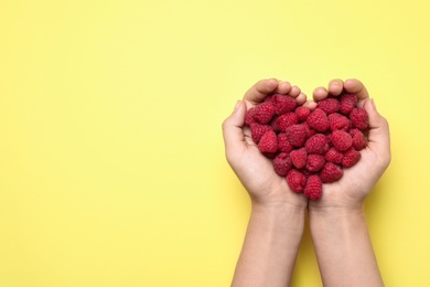 Photo of Woman holding delicious ripe raspberries on yellow background, top view. Space for text