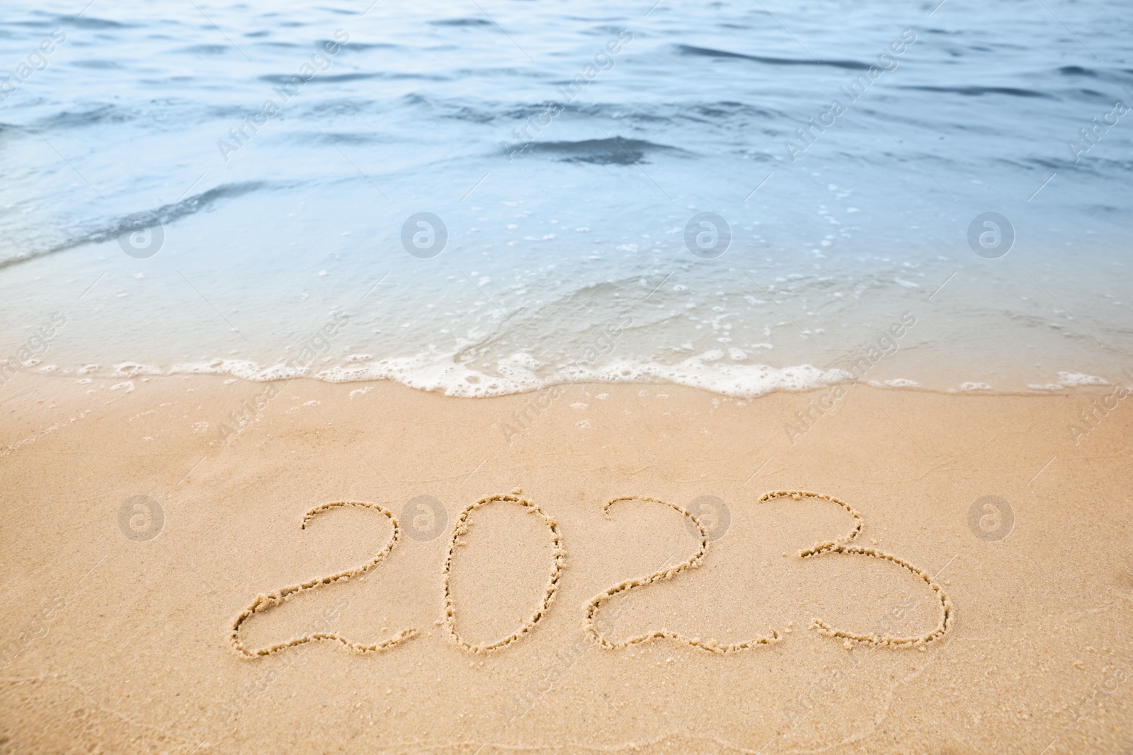 Photo of Sandy beach with written 2023 washed by sea. Happy New Year