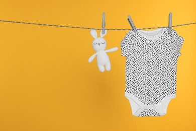 Photo of Baby onesie and bunny toy drying on laundry line against orange background, space for text