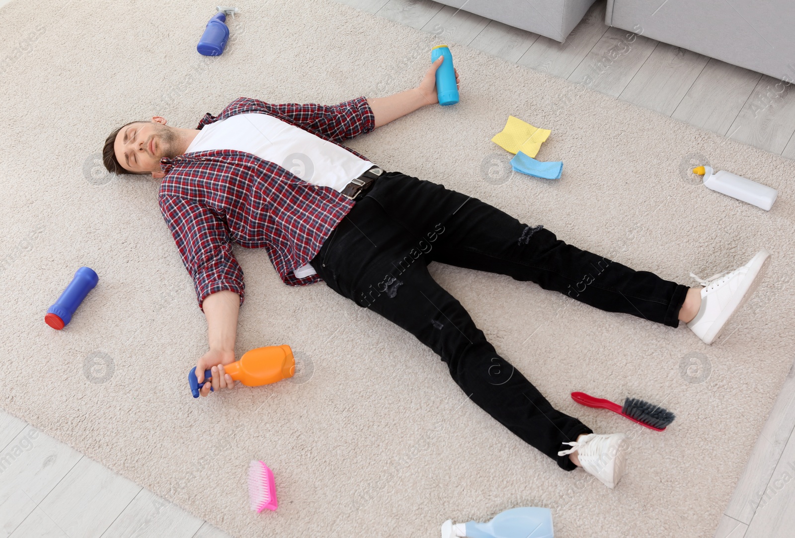 Photo of Tired man lying on carpet surrounded by cleaning supplies