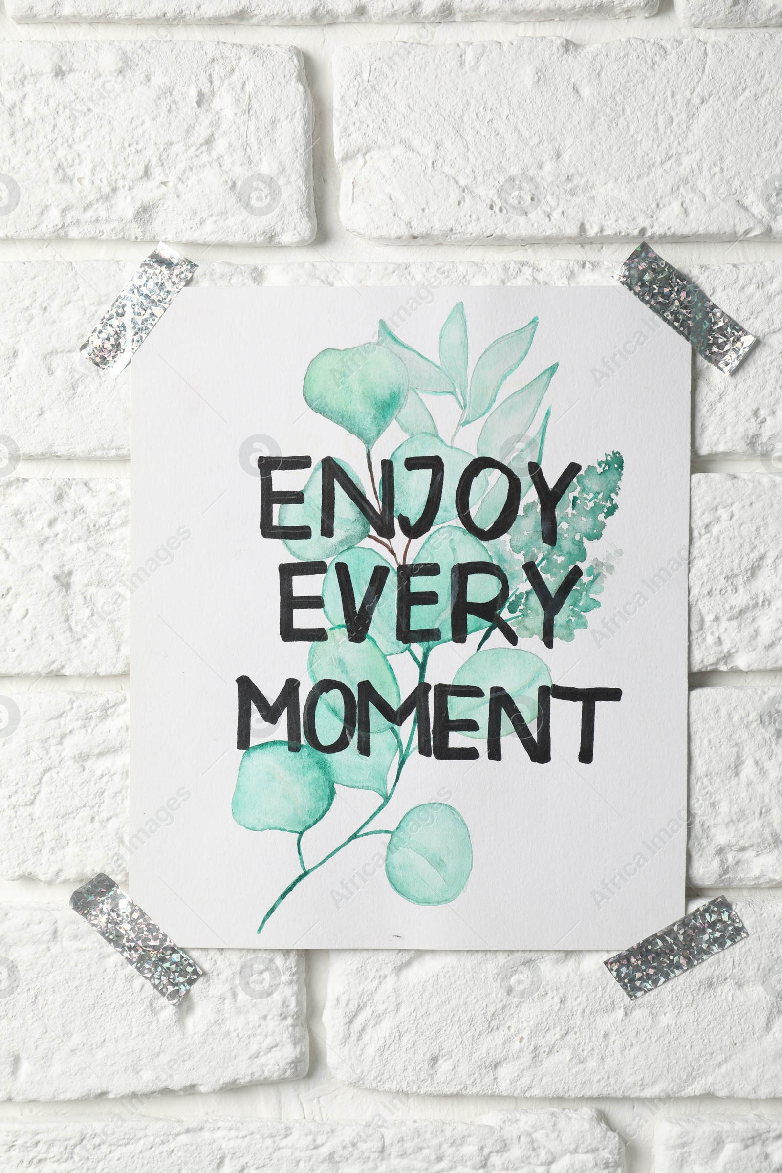 Photo of Card with phrase Enjoy Every Moment attached on white brick wall