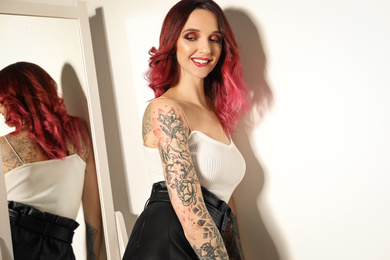 Photo of Beautiful woman with tattoos on body near mirror indoors