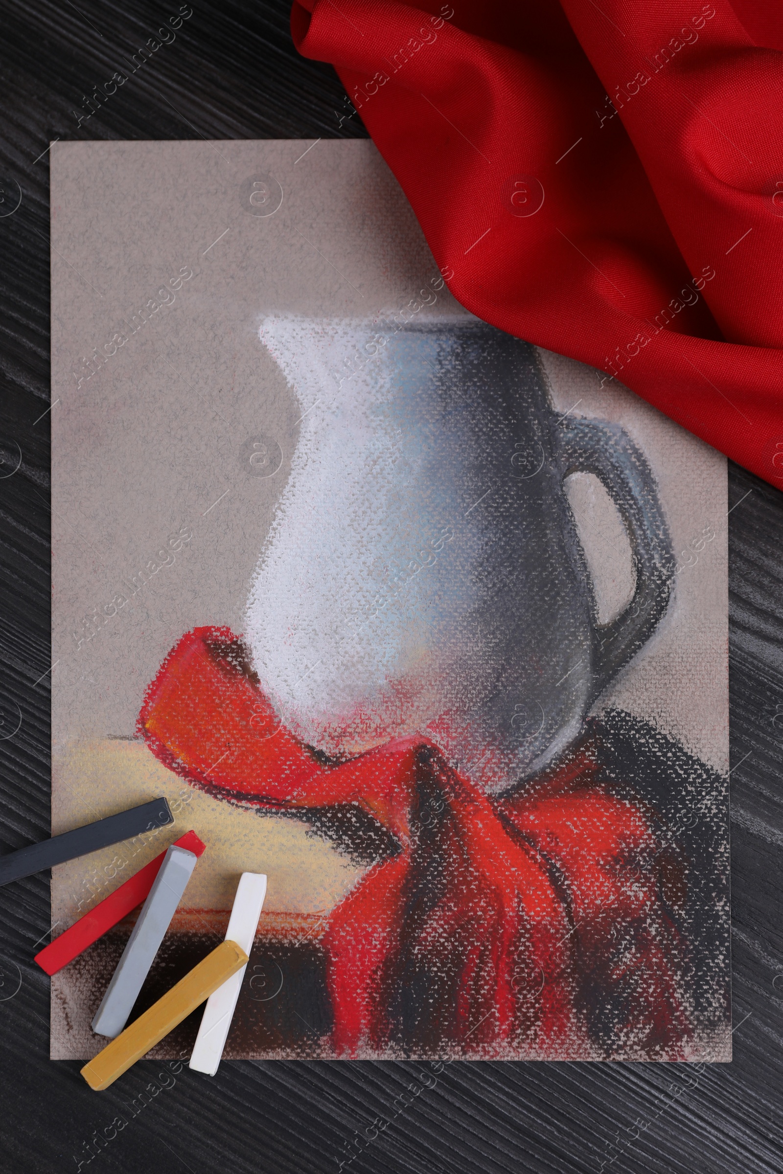 Photo of Colorful chalk pastels and beautiful painting of jug on black wooden table, flat lay