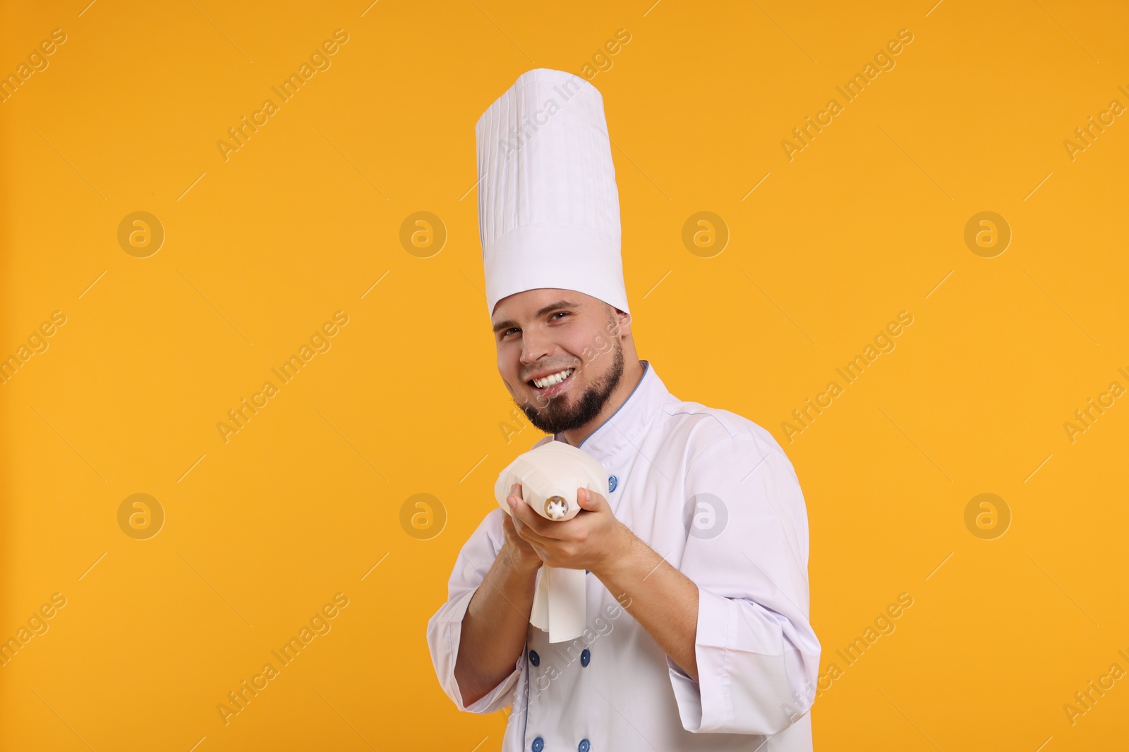 Photo of Happy professional confectioner in uniform holding piping bag on yellow background