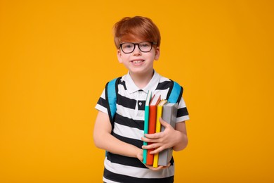 Happy schoolboy with backpack and books on orange background