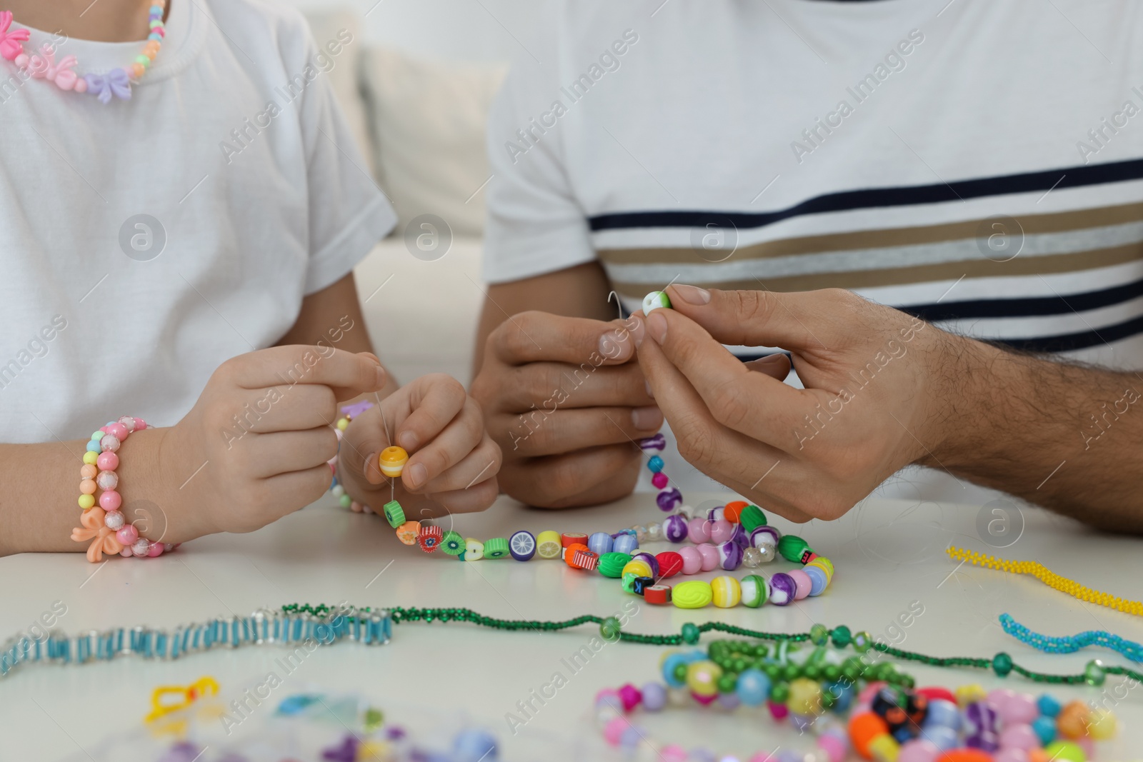 Photo of Father with his daughter making beaded jewelry at table, closeup