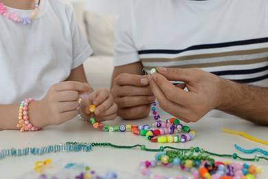 Photo of Father with his daughter making beaded jewelry at table, closeup