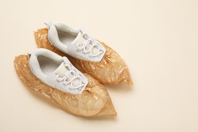 Photo of Sneakers in shoe covers on beige background, above view. Space for text